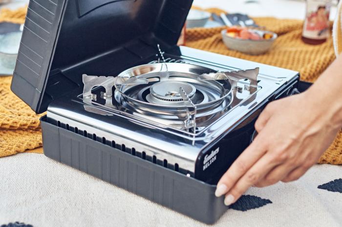 Moderne Camping-Gasherd mit Kochtopf und Lagerfeuer im Hintergrund