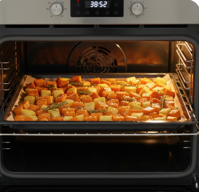 Eine Nahaufnahme von Händen, die mit einem Holzlöffel gewürfeltes Gemüse in einer Edelstahlschüssel vermengen. Im Hintergrund stehen eine Flasche Olivenöl und ein Glas Honig auf einer Holzoberfläche.