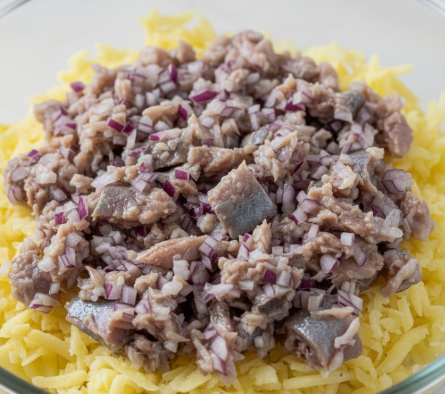 Frisch geriebene Kartoffeln als erste Schicht in einer Glasschüssel für das Schuba-Rezept, um die luftige Struktur des Schichtsalats zu bewahren.