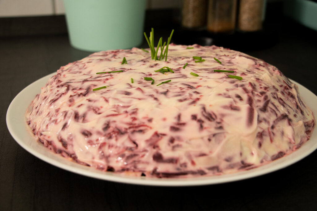 Die oberste Schicht des Schuba-Salats aus fein geriebener Roter Bete, die mit einer glatt gestrichenen Schicht Mayonnaise bedeckt ist, wodurch eine charakteristische rosa-violette Oberfläche entsteht.