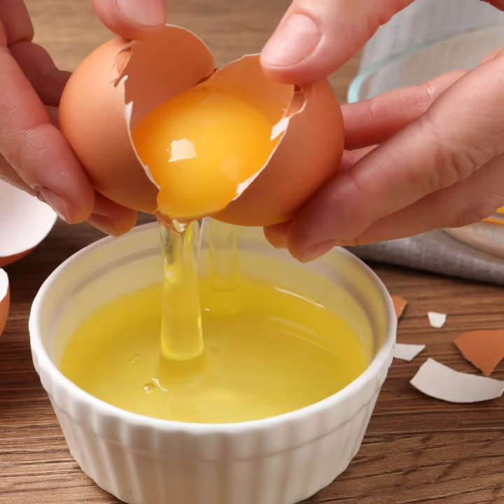 Eine Person trennt Eigelb von Eiweiß über einer weißen Schale.
