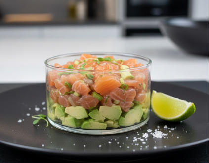 Elegante Vorspeise: Frisches Lachstatar auf Avocado-Creme, serviert in einem Glasring mit Limette und Meersalz auf einem dunklen Teller.